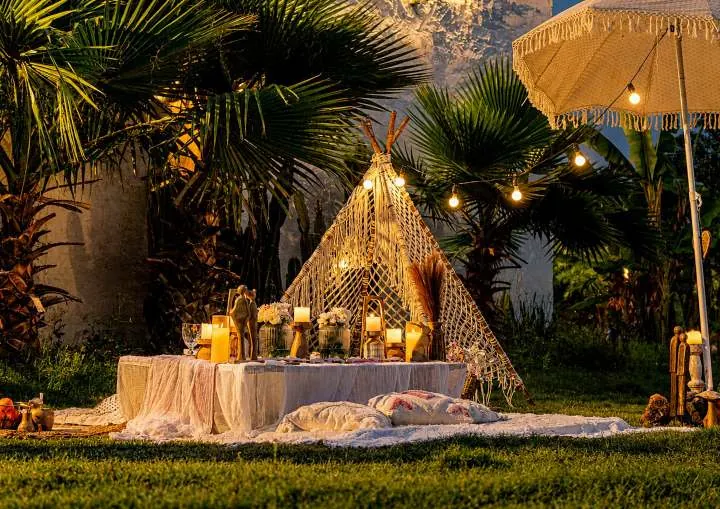 A macramé tent picnic setup lit with candles and fairy lights at dusk